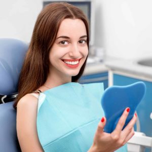 young woman looking at smile in mirror at dentist
